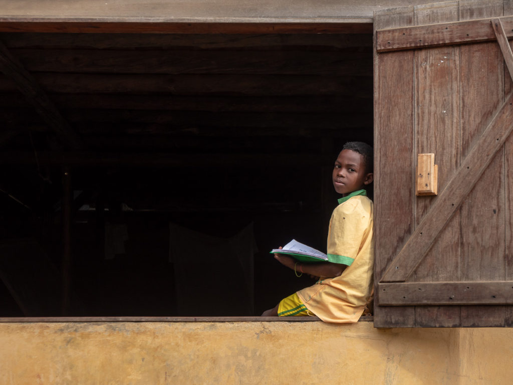 Child reading text sitting in window of school in Madagascar