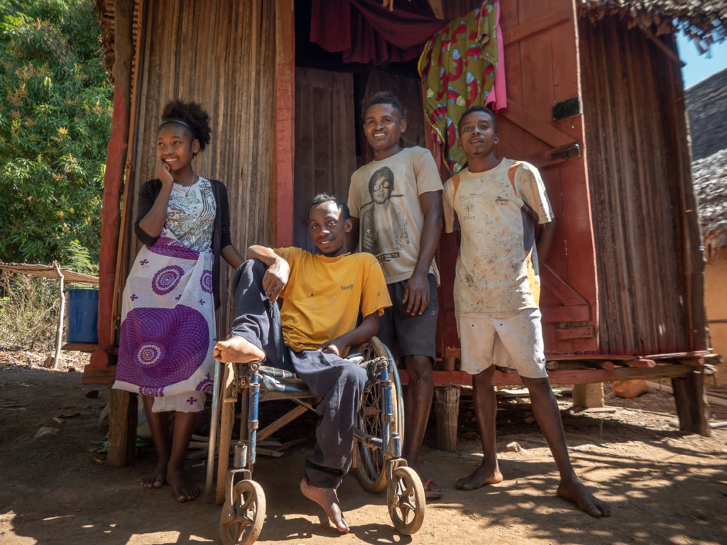 Man in a wheel chair surrounded by three smiling friends in front of bamboo house on Nosy Komba Madagacar