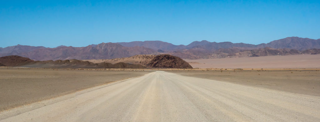 Gravel road headed toward purple mountains in Namibia