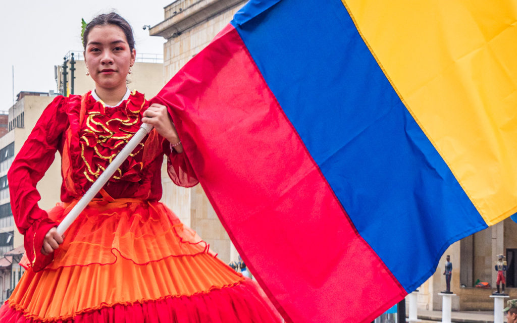 Girl dressed in historical costume carrying Colombia Flag in Simon Bolivar Parade 2019 Bogota
