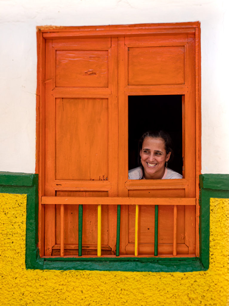 Woman smiling from frame of colorful green, yellow and orange windowsill in Jericó, Colombia