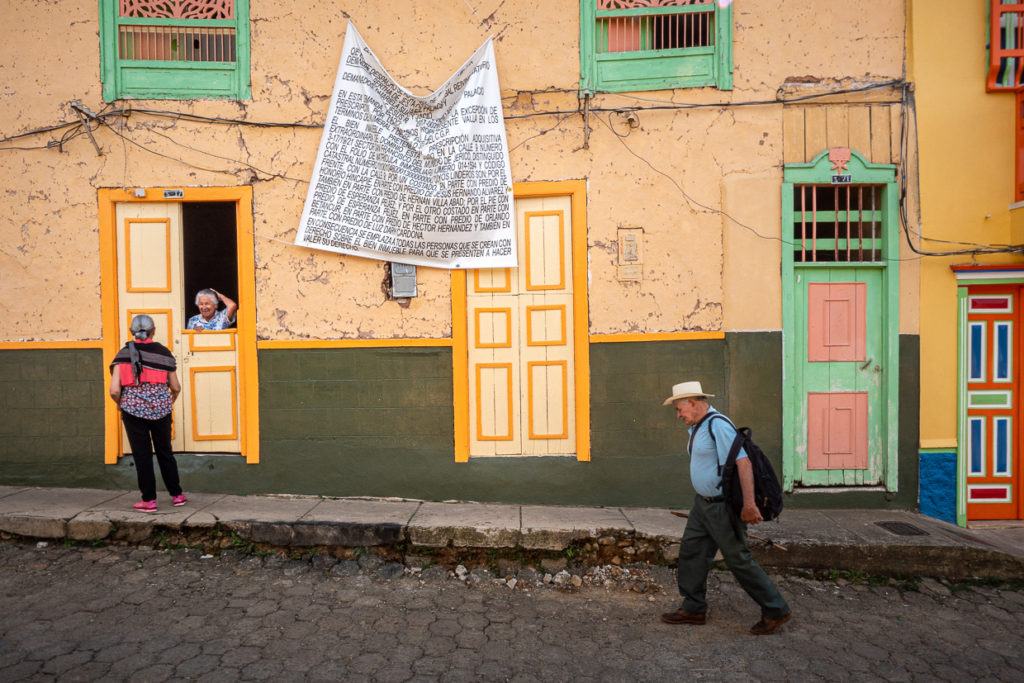 Man walking along coloful Jericó, Colombia street was women meet at nearby windowsill
