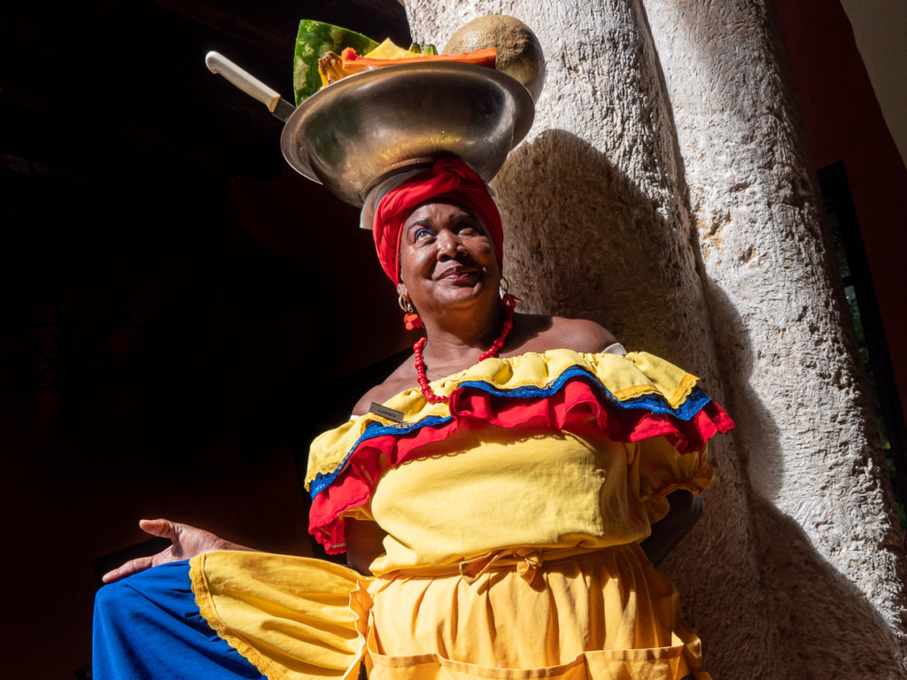 Palenquera with fruit on head in a rainbow of colorful African clothing adorned with flourishes holding wide skirt