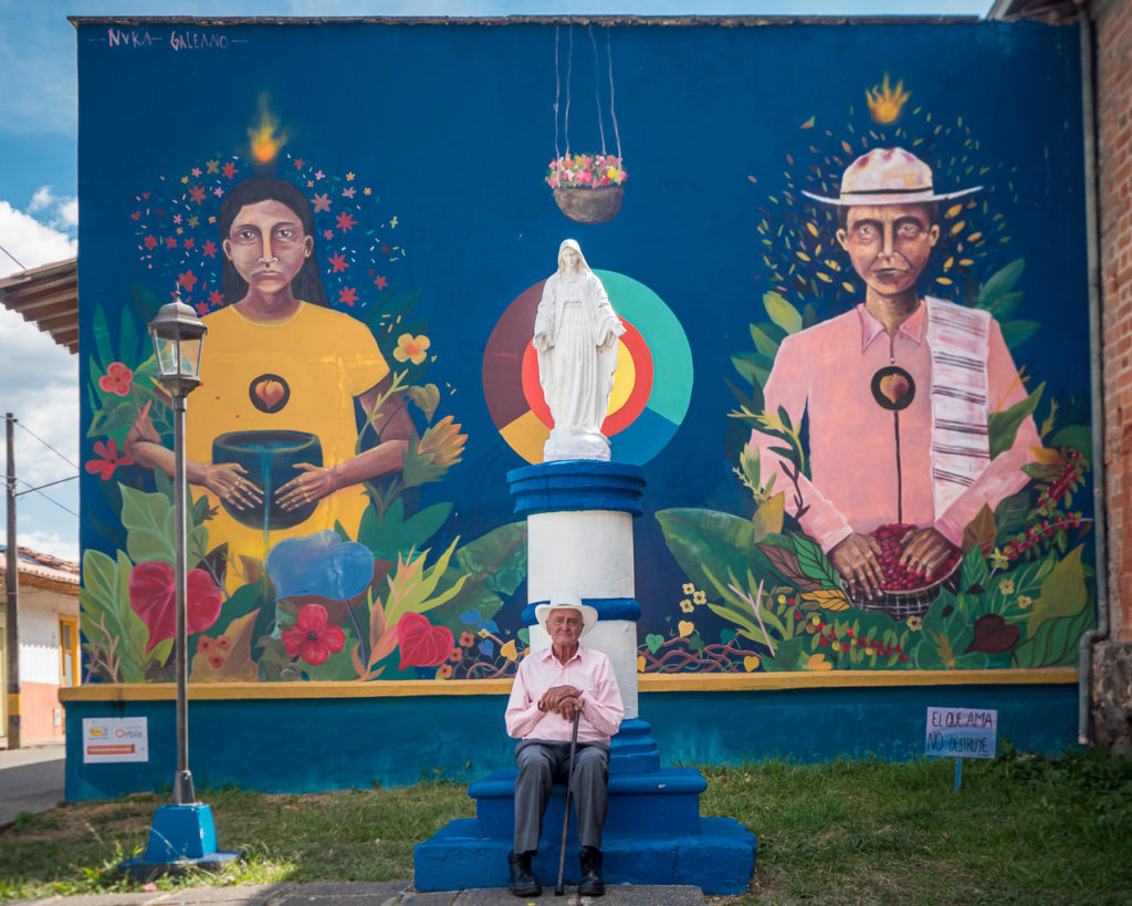 Man sits in front of statue and street art reflecting Colombia's heritage on road to Jericó