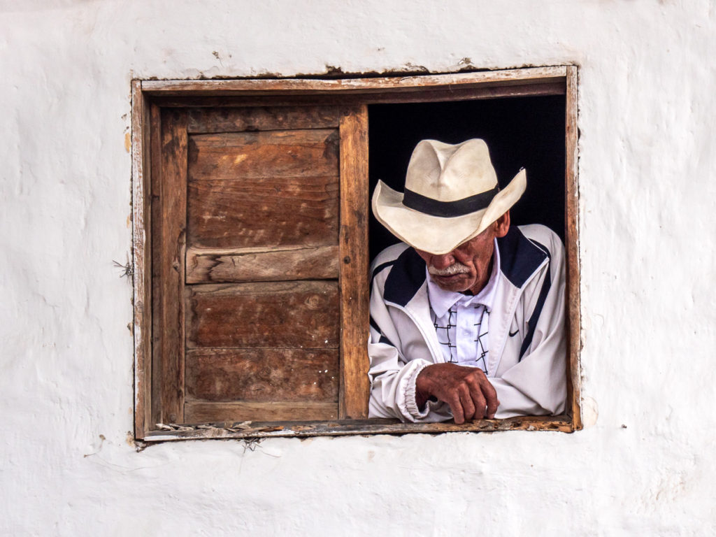 Cowboy looks downward to street below from wooden window in whitewashed building Villa de Leyva, Colombia